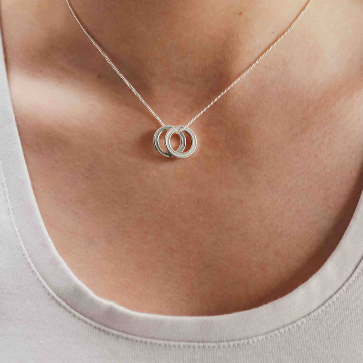Silver necklace with interlocking rings on a person wearing a white top.