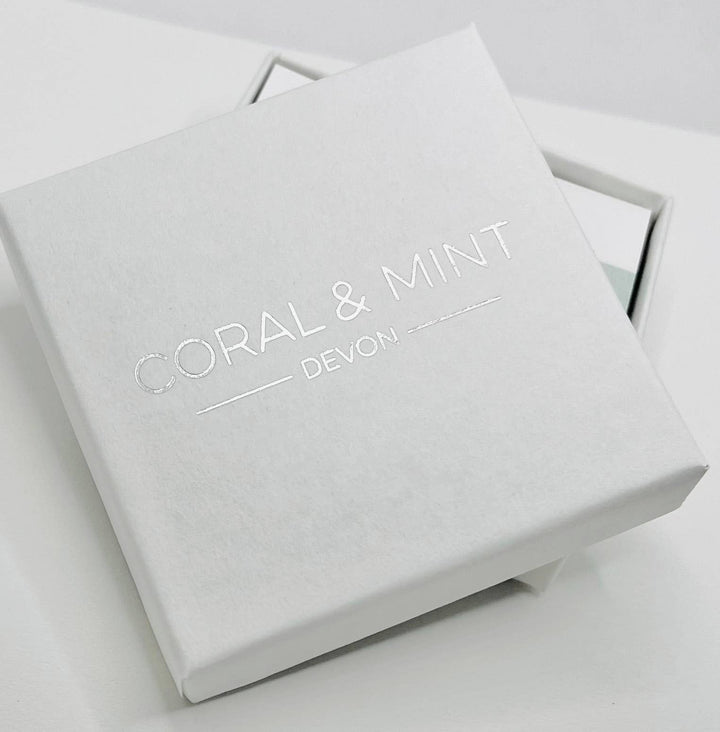 White jewelry box with 'Coral & Mint Devon' branding on a light gray background