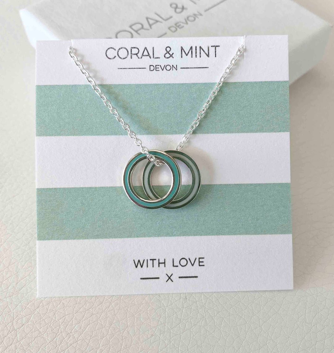 Necklace with interlocking rings on a 'Coral & Mint Devon' branded card.