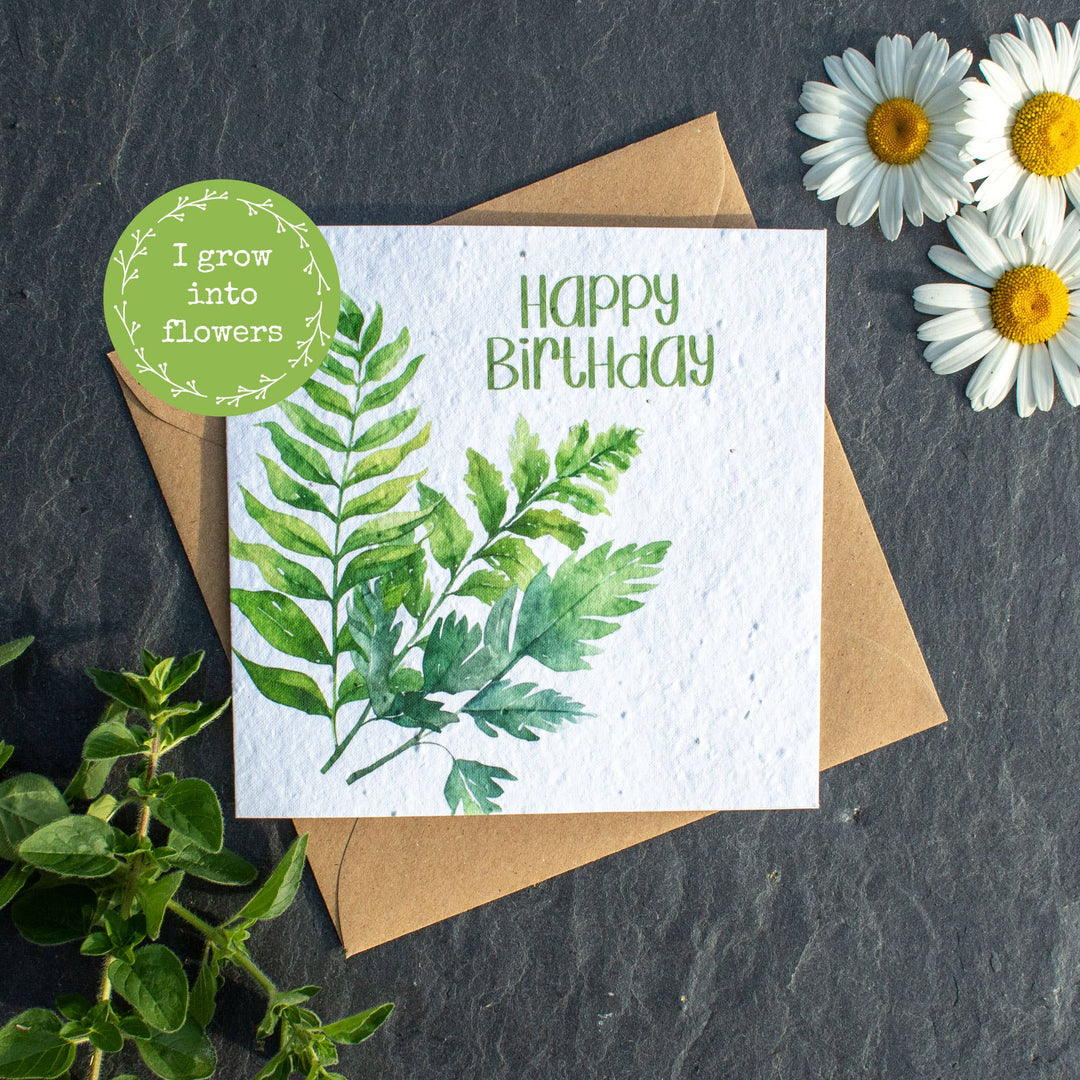 Birthday card with greenery design, envelope, and daisies on a dark surface