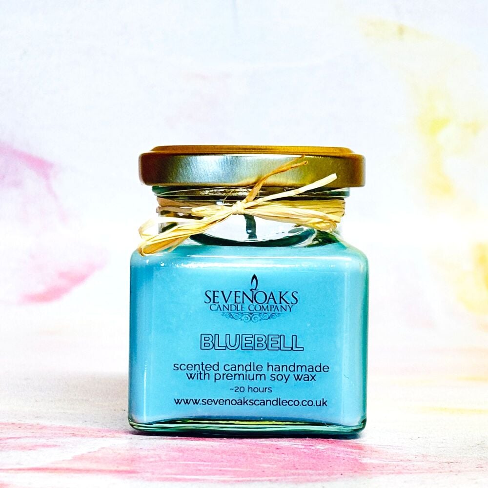 A blue scented candle with a label reading 'Bluebell', handmade with premium soy wax, presented in a small glass jar with a gold lid and tied with a ribbon.