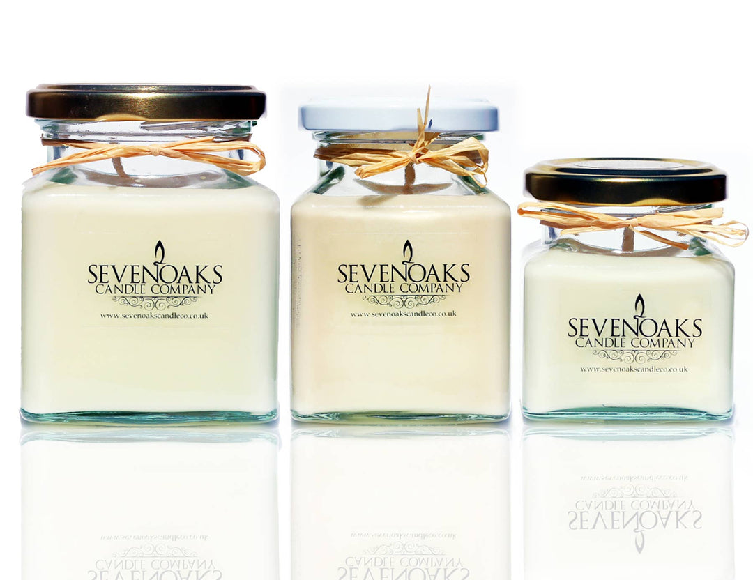 Three glass jars with white candles inside, each adorned with a raffia ribbon and a label reading 'SEVENOAKS'. The jars vary in size and are displayed against a white background.