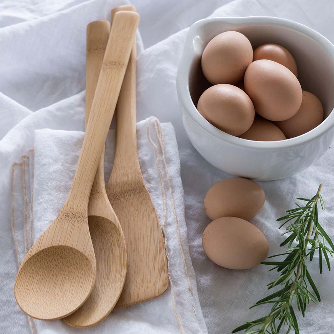 Wooden spoons on a white cloth with a bowl of eggs and rosemary.