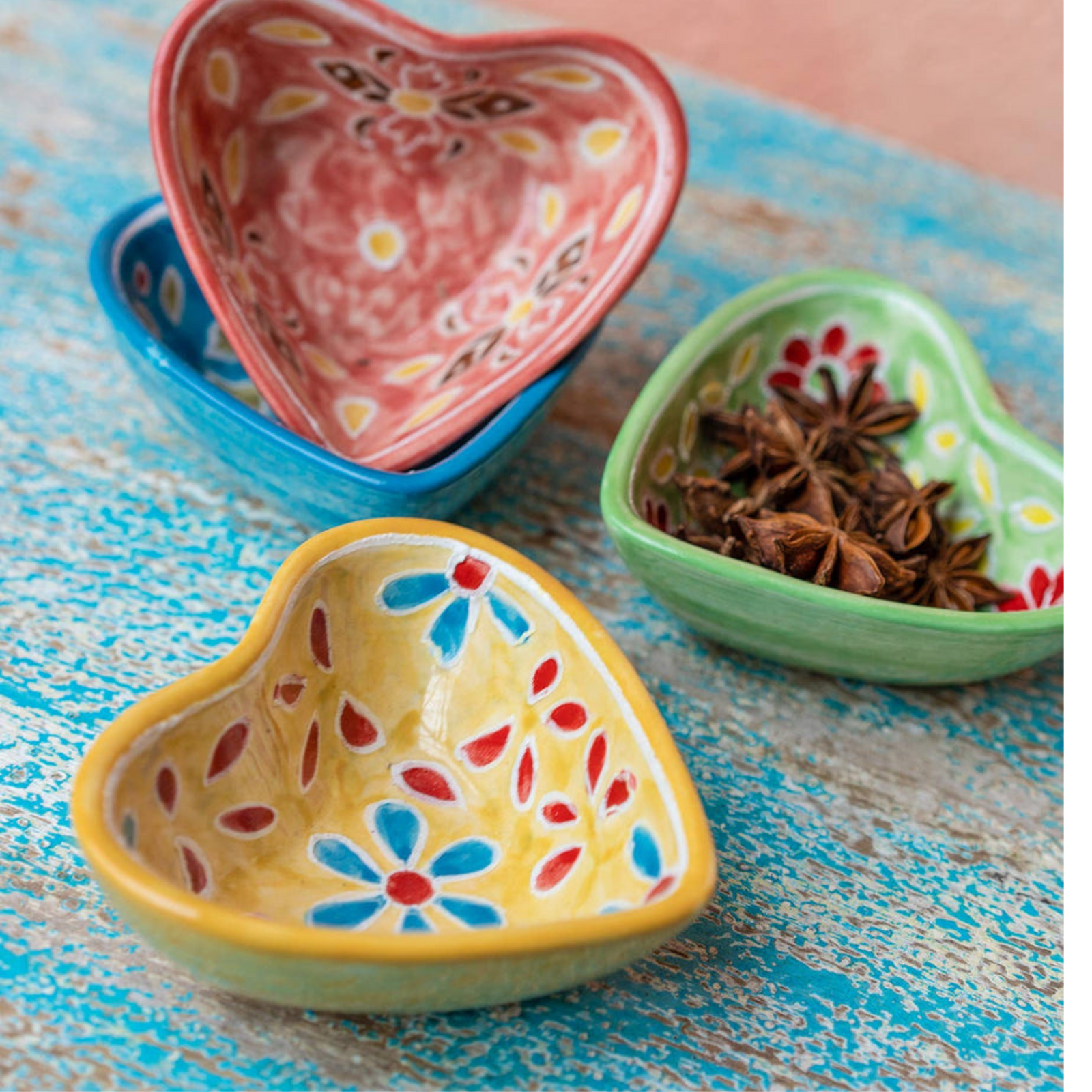 Hand painted ceramic heart-shaped dishes in different colors with floral patterns. Red, Blue, Yellow, Green.