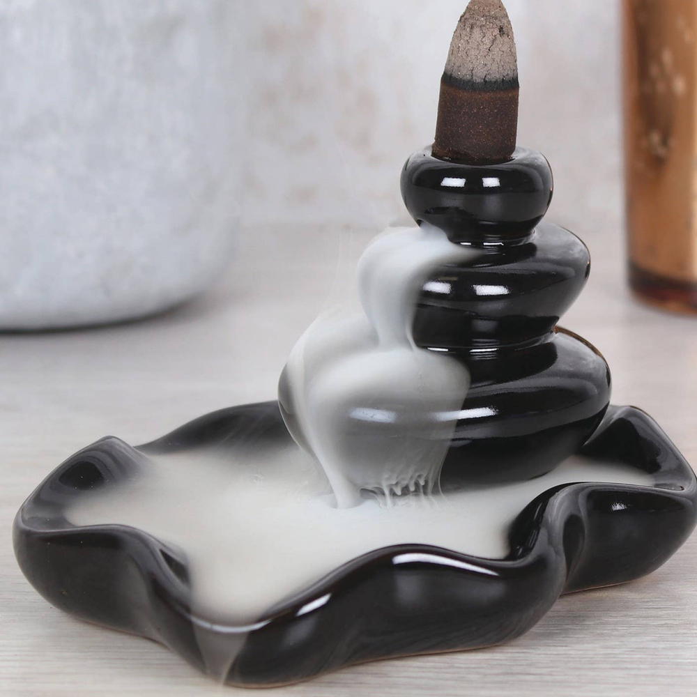 Black and white ceramic incense burner with a lit incense stick on a light background