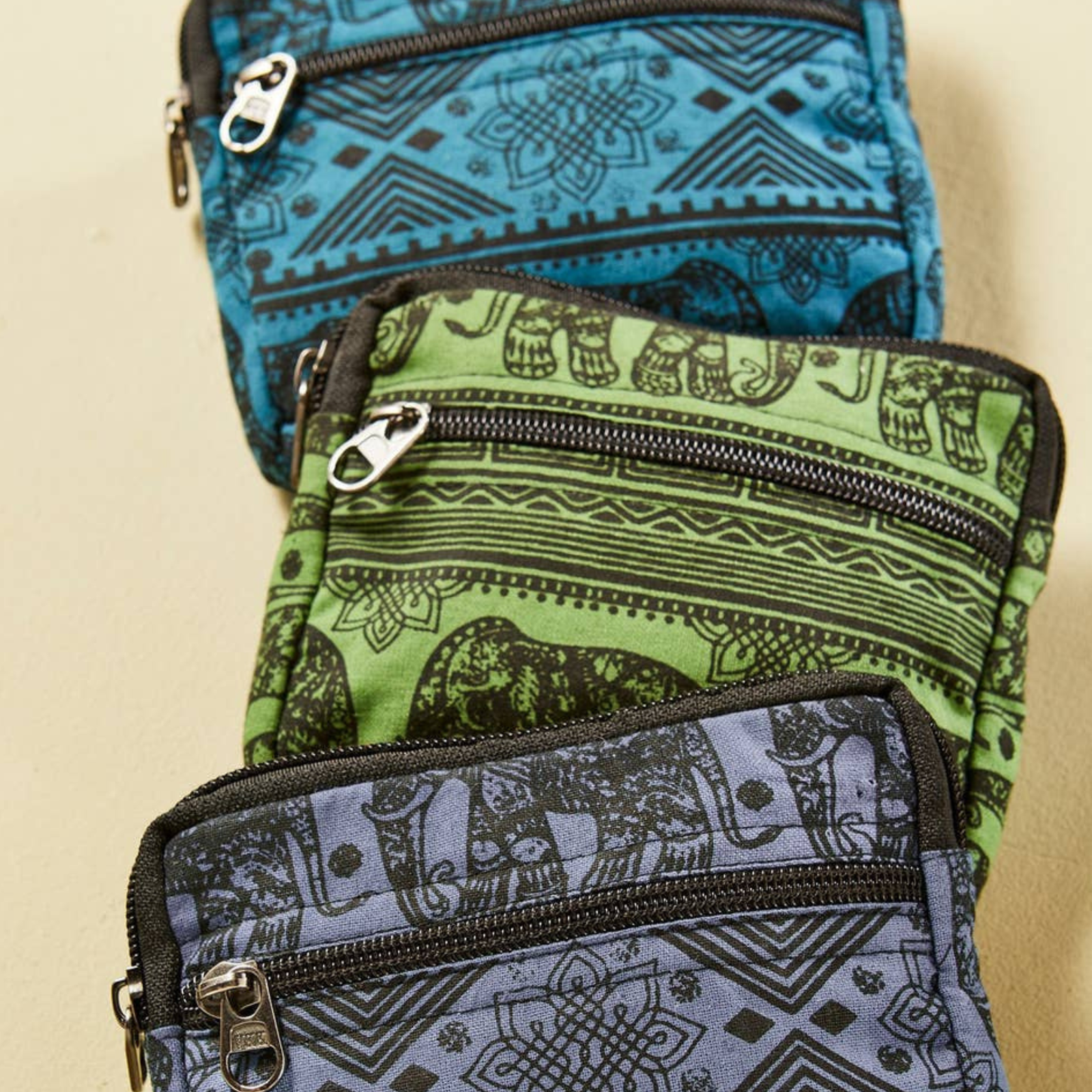 Three patterned coin purses, Blue, Green and purple with a black printed elephant design stacked on a beige background.