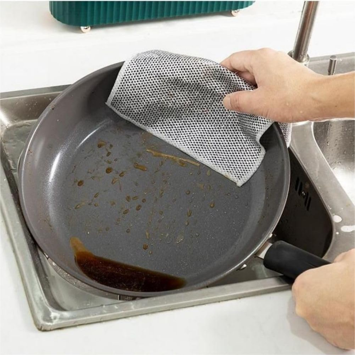 Person cleaning a greasy frying pan with a double sided steel wire Dishcloth in a sink.