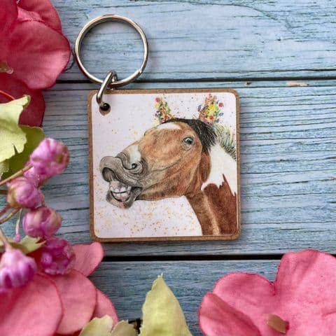 Keychain with a horse illustration on a wooden background surrounded by pink flowers.