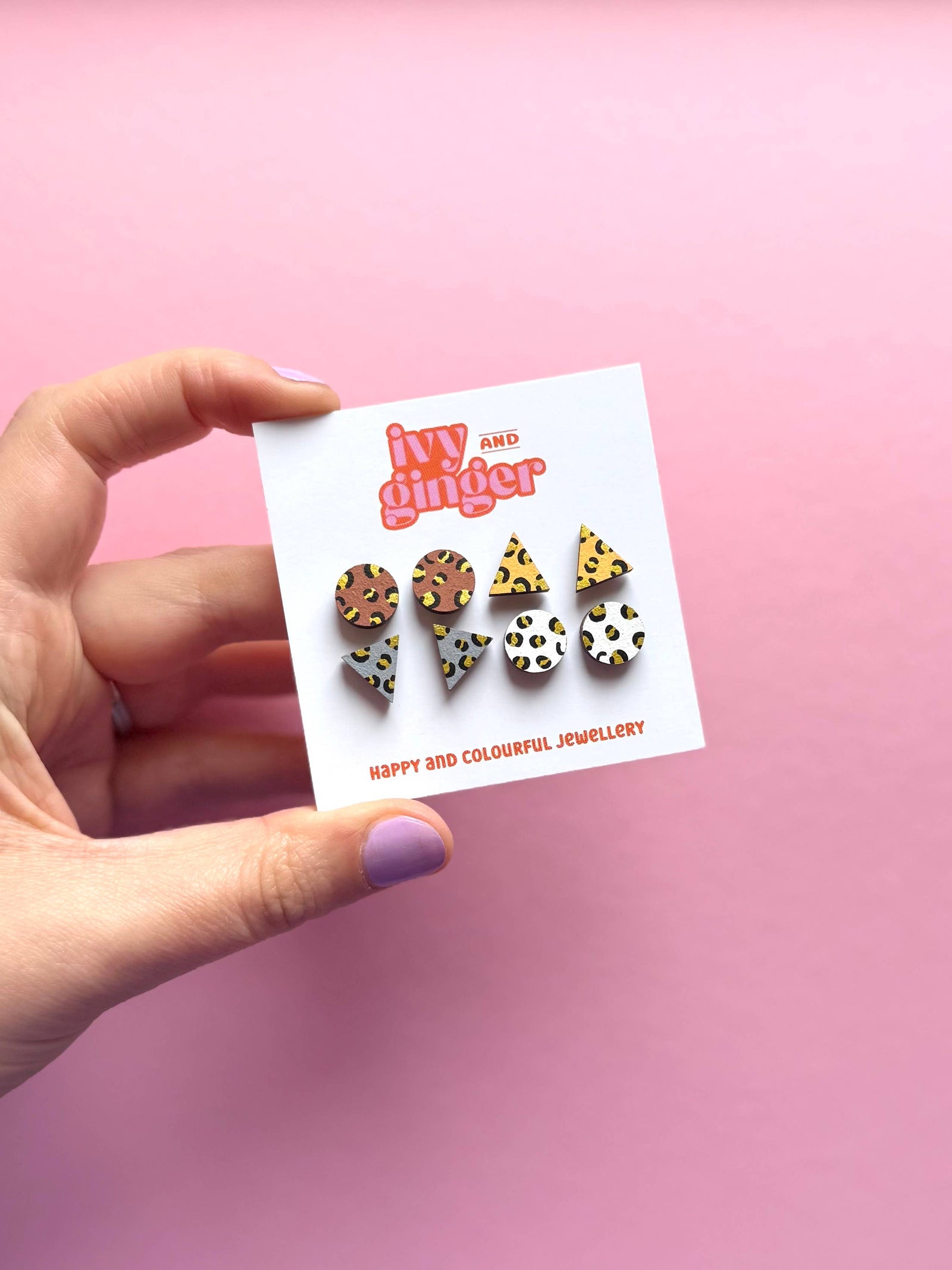 Hand holding a card with colourful leopard print earrings against a pink background