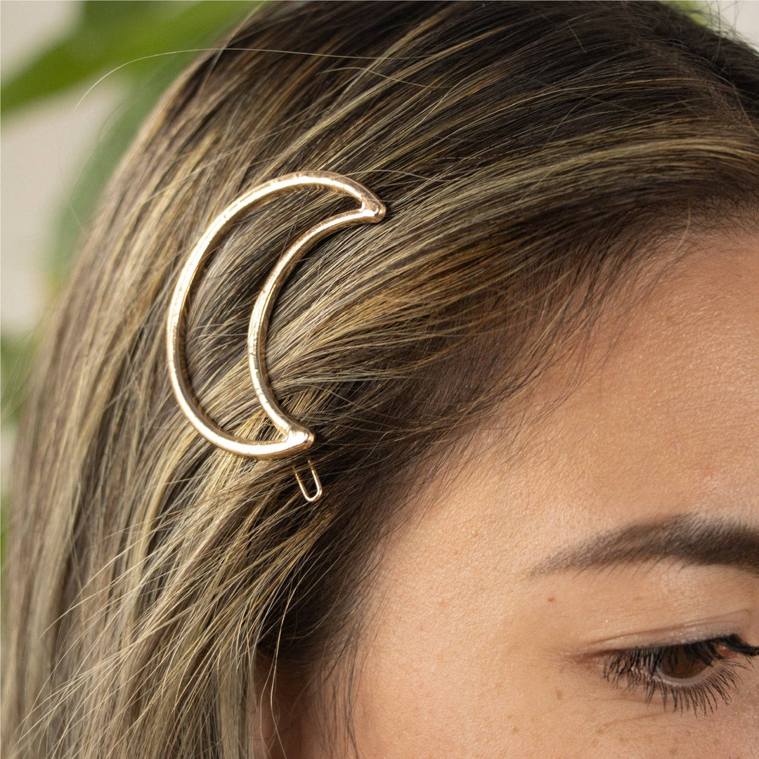Gold crescent moon hair clip worn by a person with blurred greenery in the background