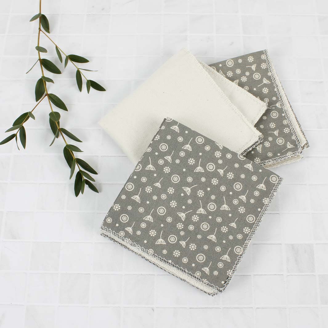 Three grey reusable wipes with white patterns on a light wooden surface.