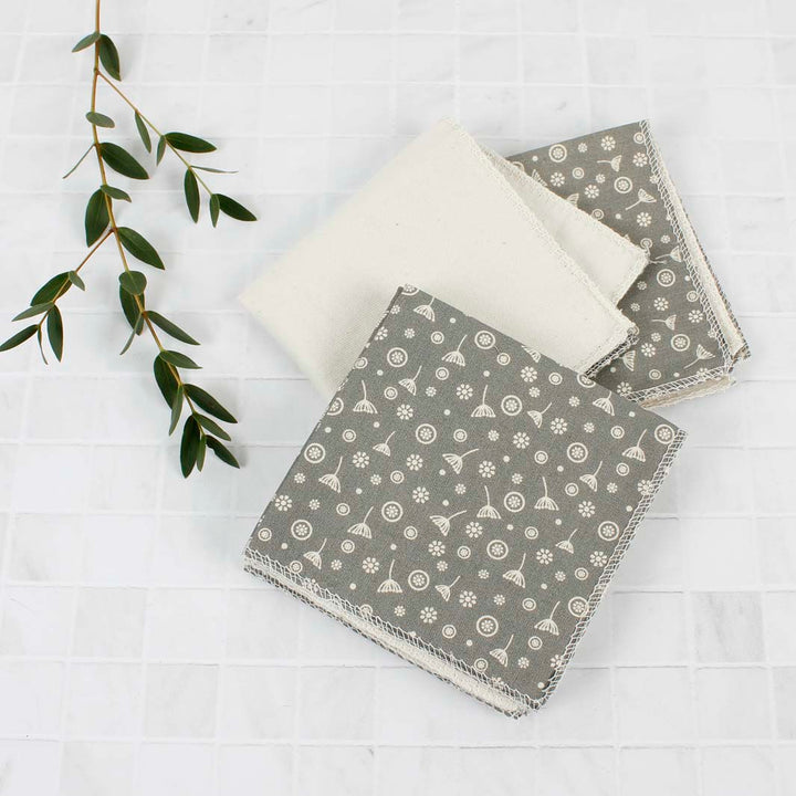 Three grey reusable wipes with white patterns on a light wooden surface.