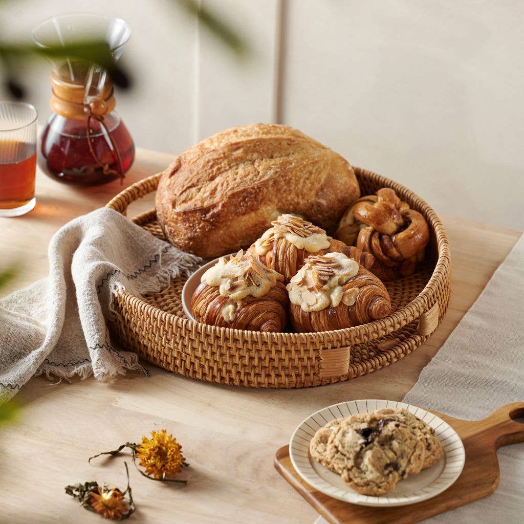 Basket of bread and pastries on a wooden table with a glass of tea.