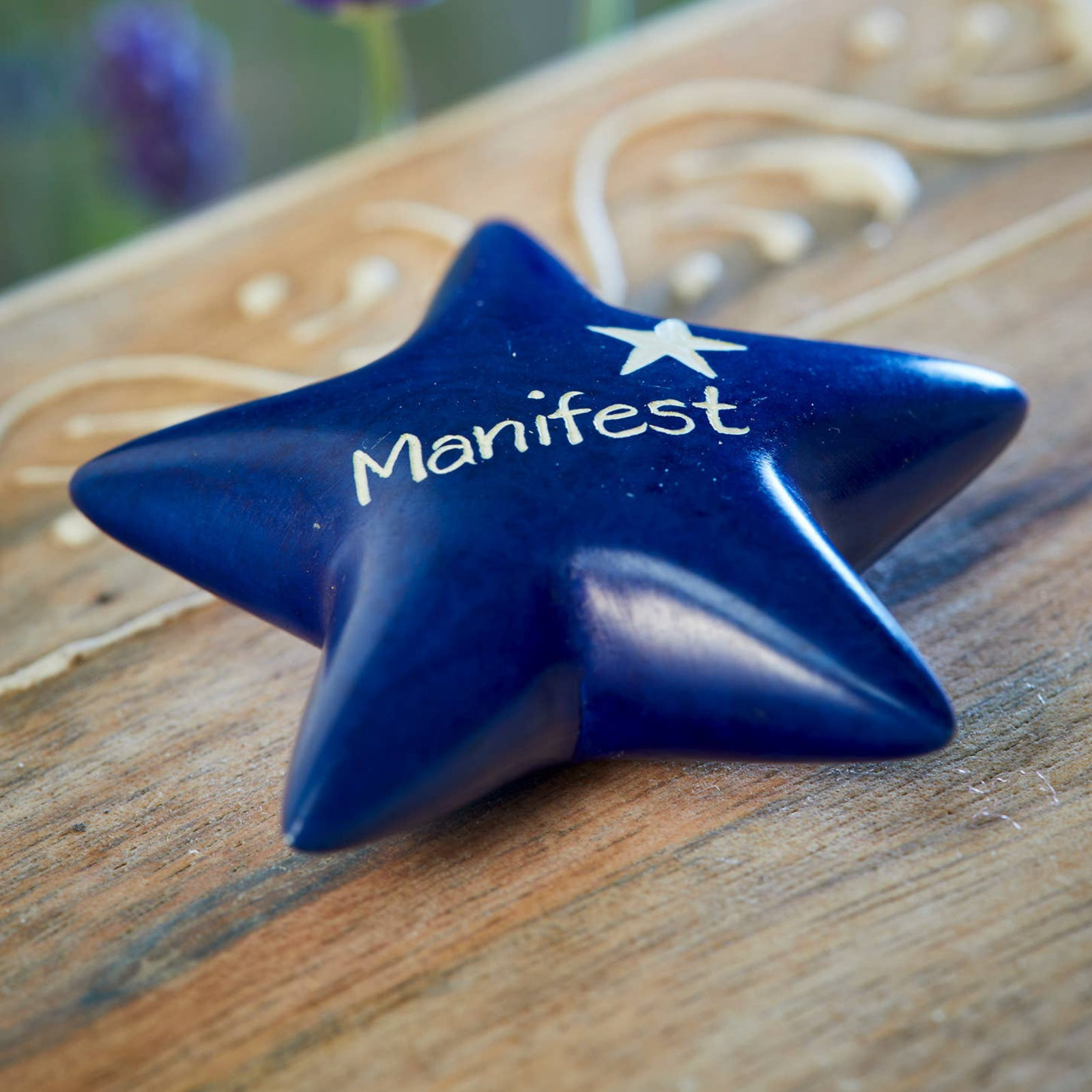 Blue star-shaped object with 'Manifest' written on it, placed on a wooden surface.