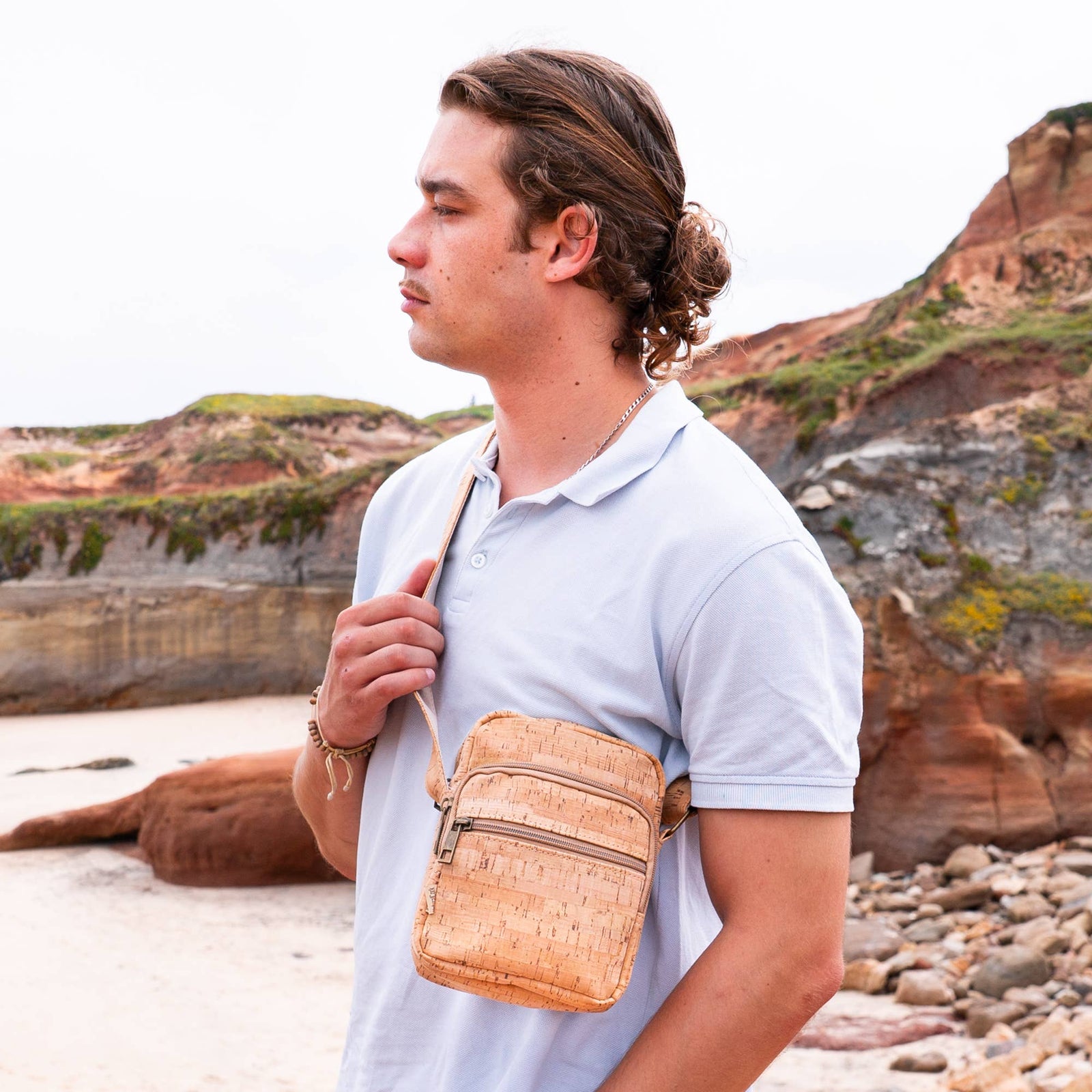 Man with a woven bag standing on a beach with cliffs in the background