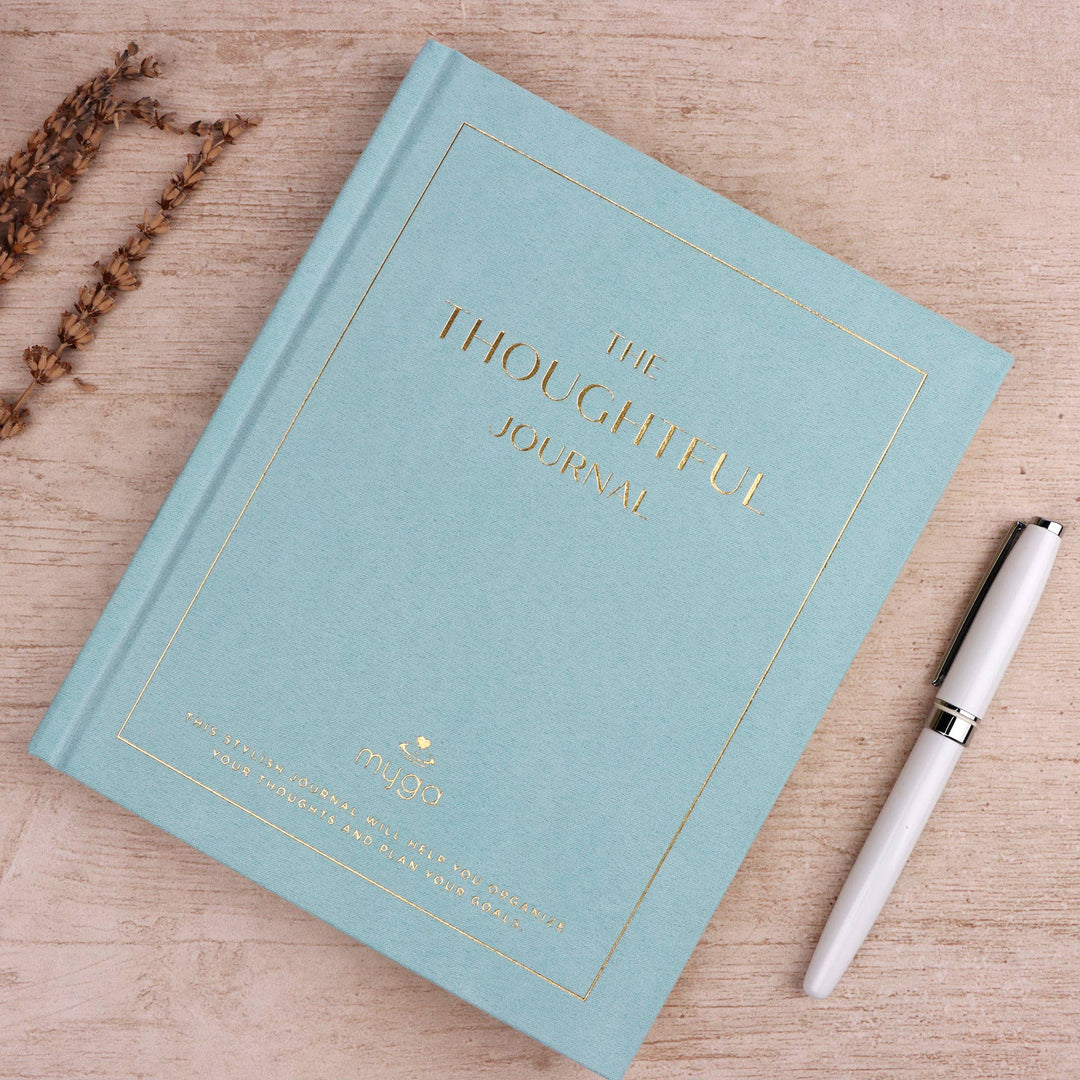 Light blue journal titled 'The Thoughtful Journal' with a white pen on a wooden surface.