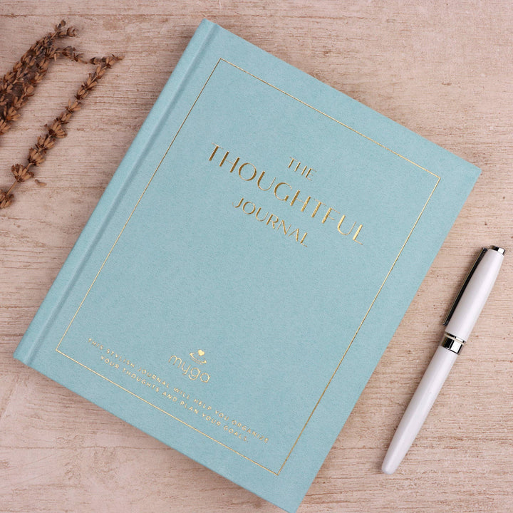 Light blue journal titled 'The Thoughtful Journal' with a white pen on a wooden surface.