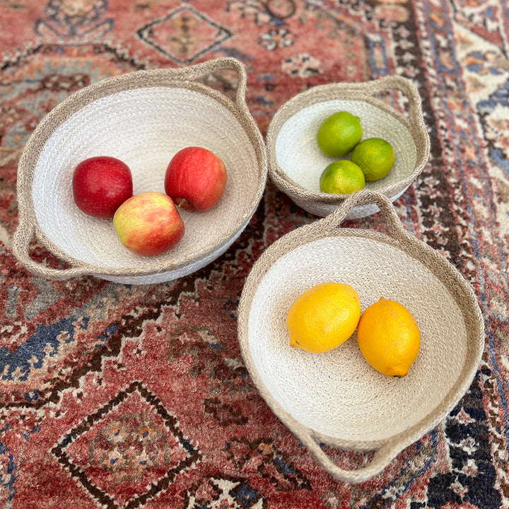 Three woven baskets cream and brown with handles with fruits on a patterned rug