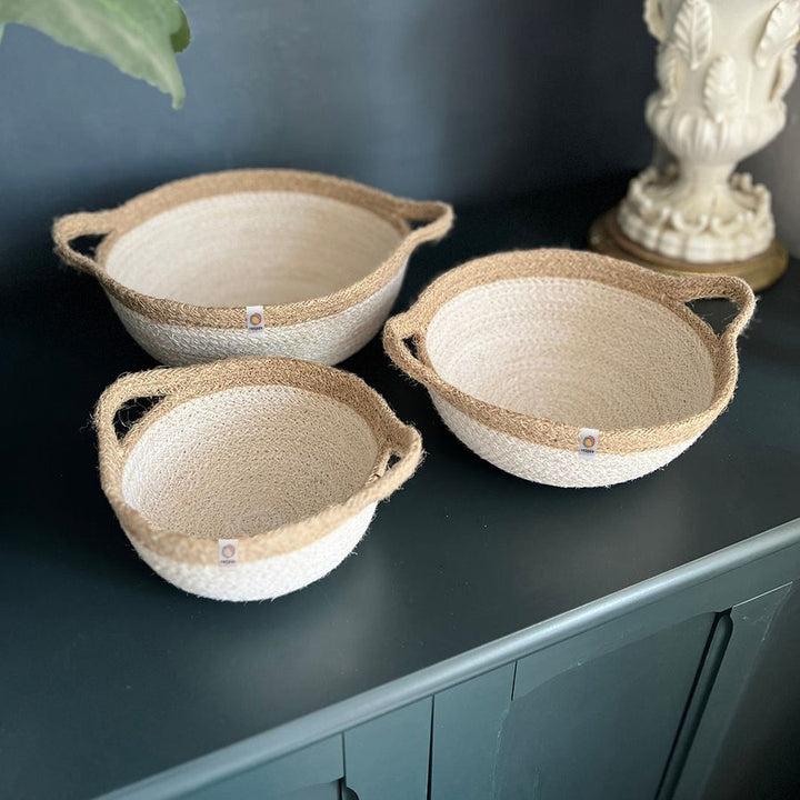 Three woven baskets in white / brown with handles on a dark surface