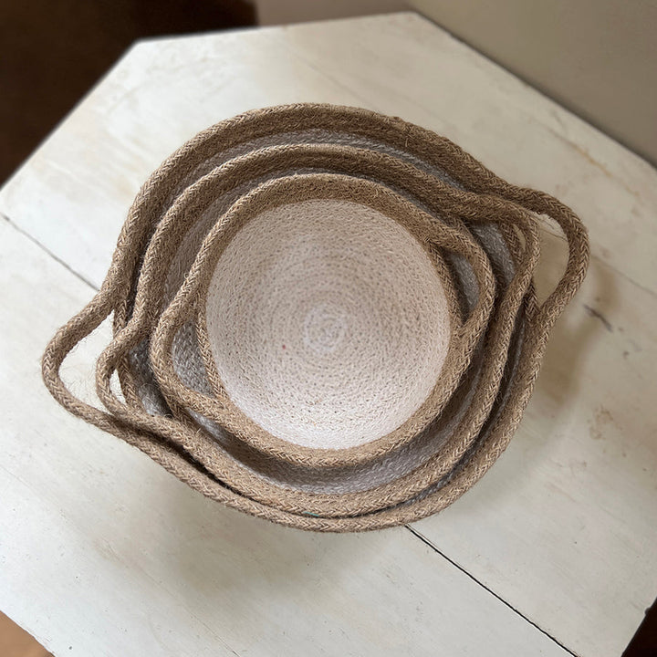 Set of woven white / brown baskets with handles stacked neatly together on a light wooden surface