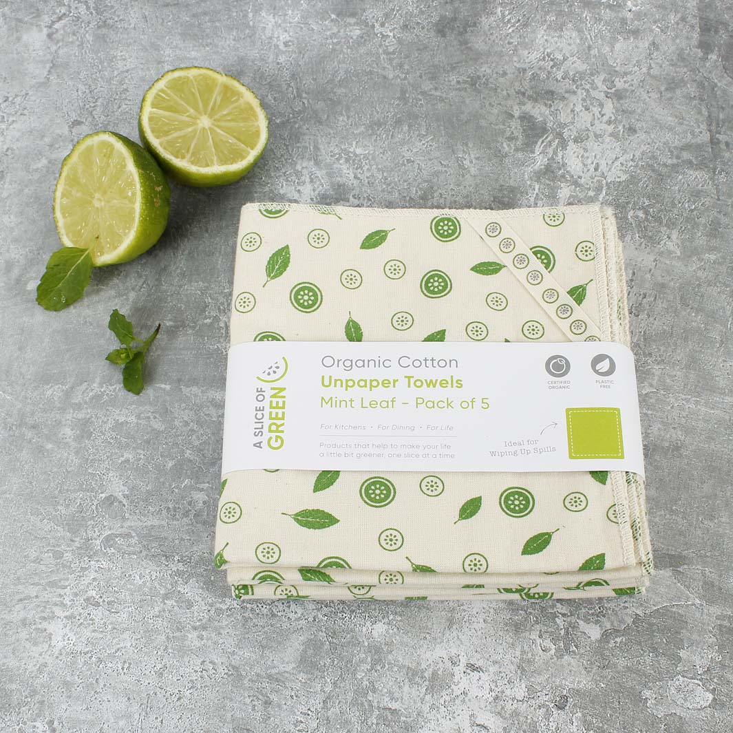 Pack of organic cotton unpaper towels with mint leaf design on a gray surface with limes and mint leaves.