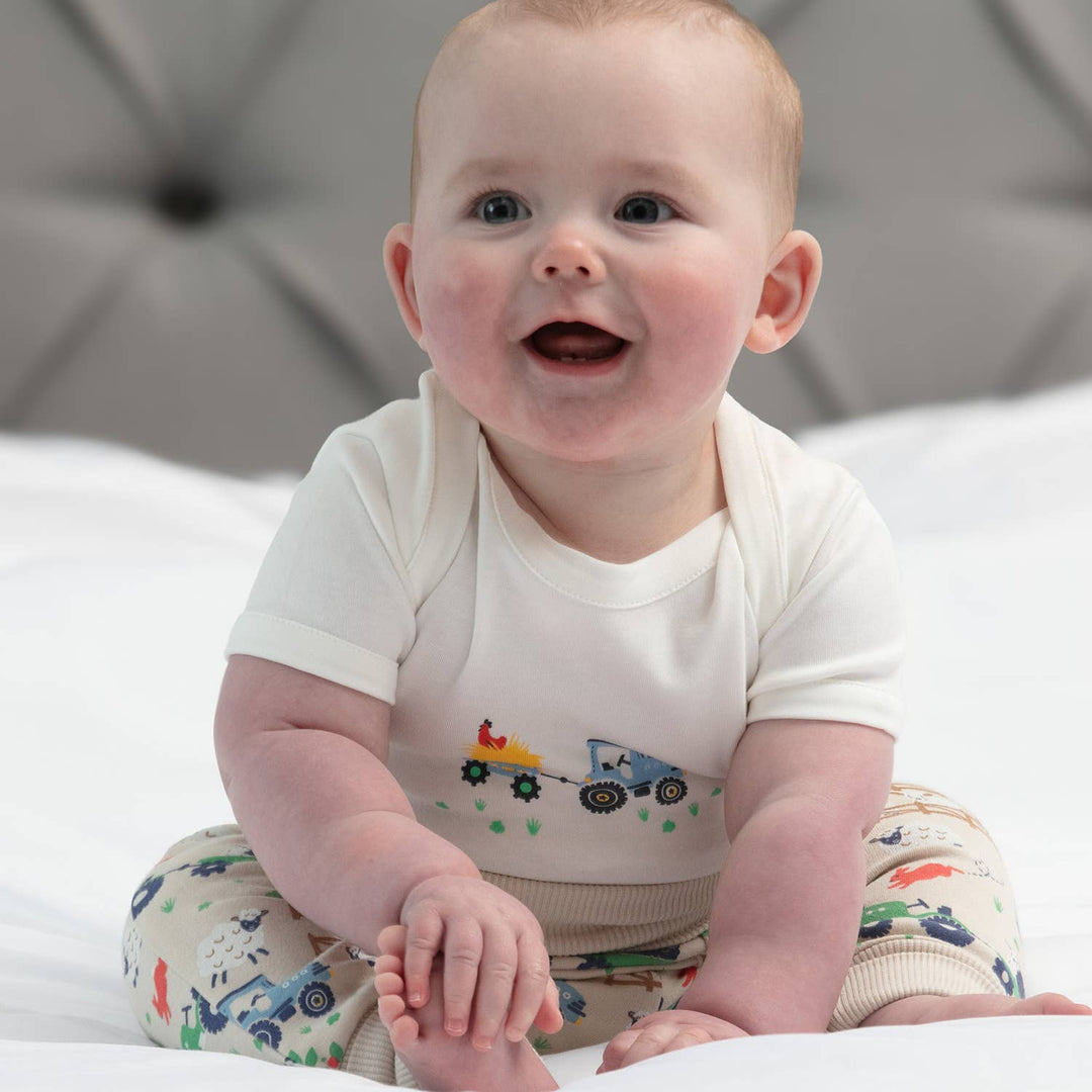 Double pack of organic cotton baby bodysuits. One bodysuit features an all-over farm print on a beige base with tractors and animals.