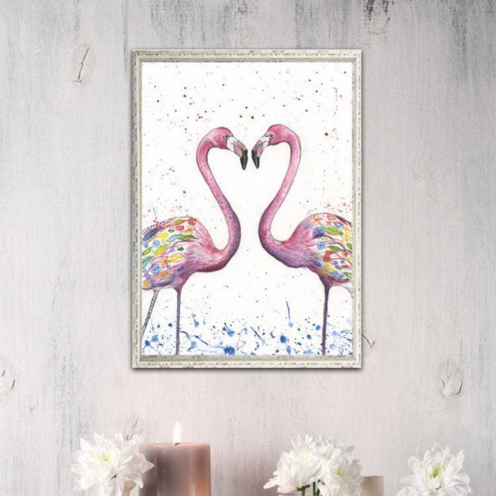 Framed artwork of two pink flamingos forming a heart shape on a light gray wall.