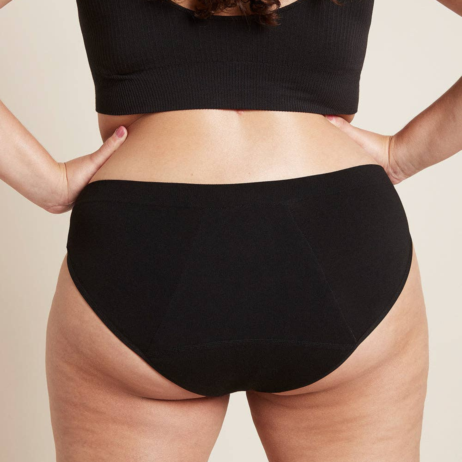 Person wearing black high-waisted underwear on a beige background