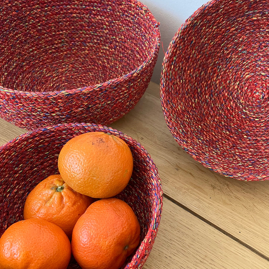 Three woven red bowls with oranges on a wooden surface