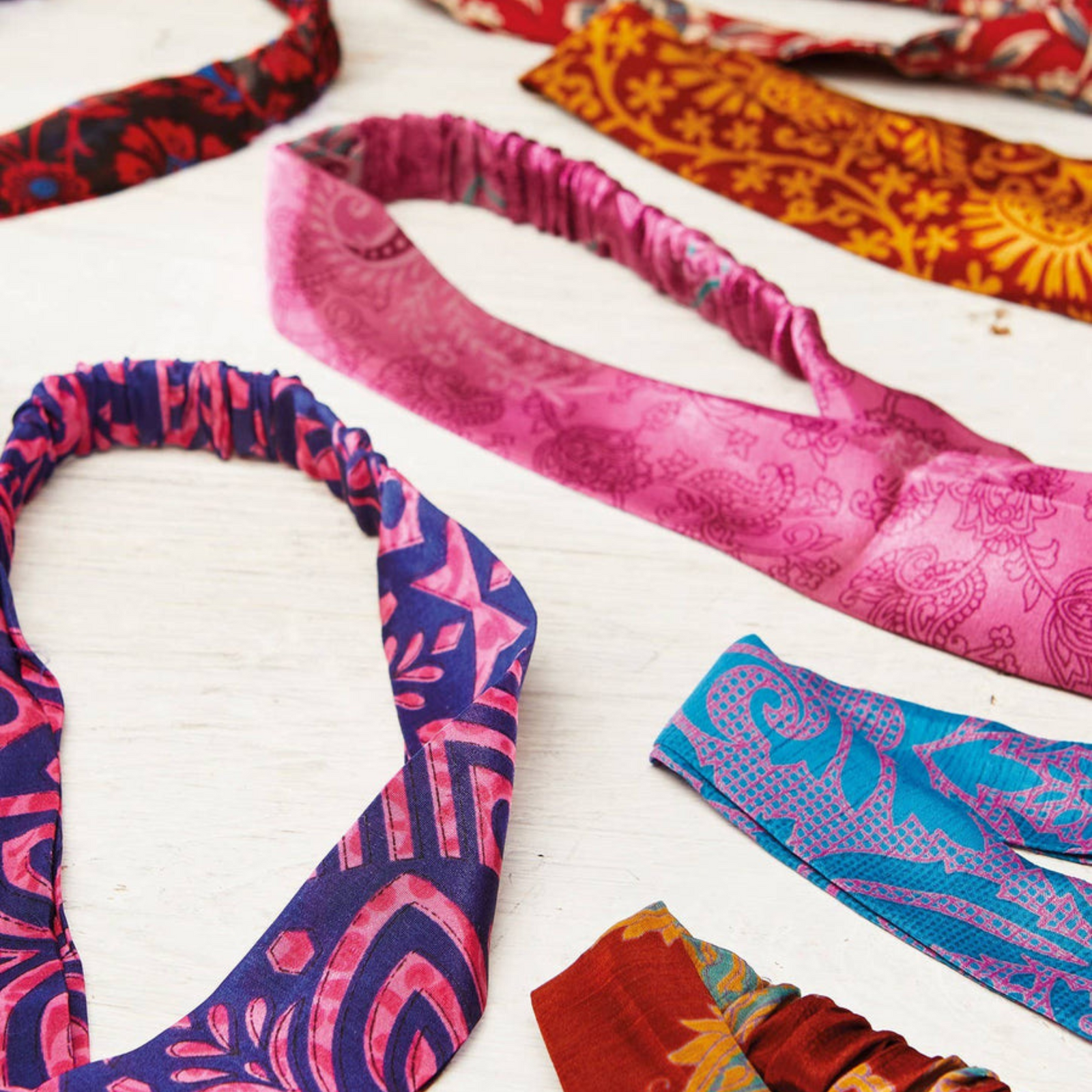 A collection of recycled sari headbands in assorted colors and patterns laid out on a white surface.