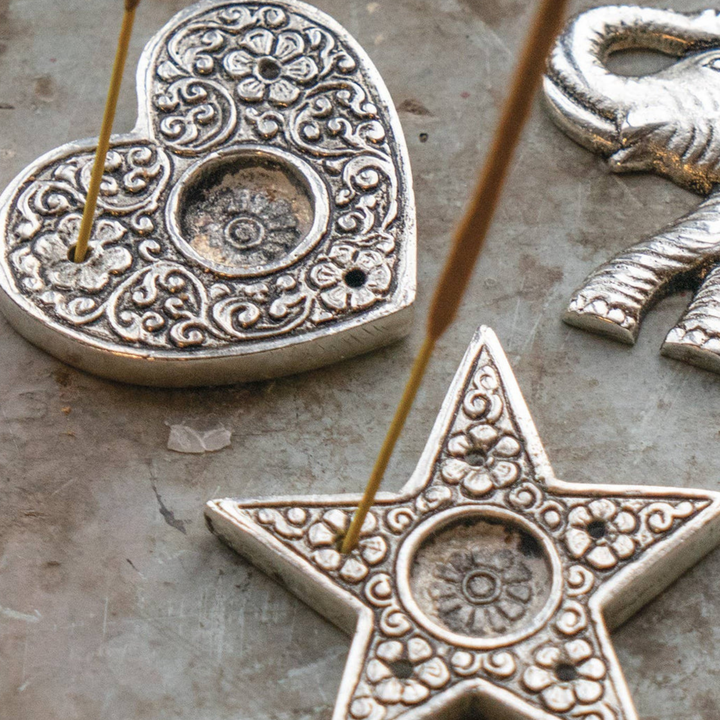 Decorative metal heart and star incense holders on a textured surface.