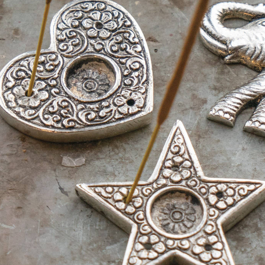 Decorative metal heart and star incense holders on a textured surface.