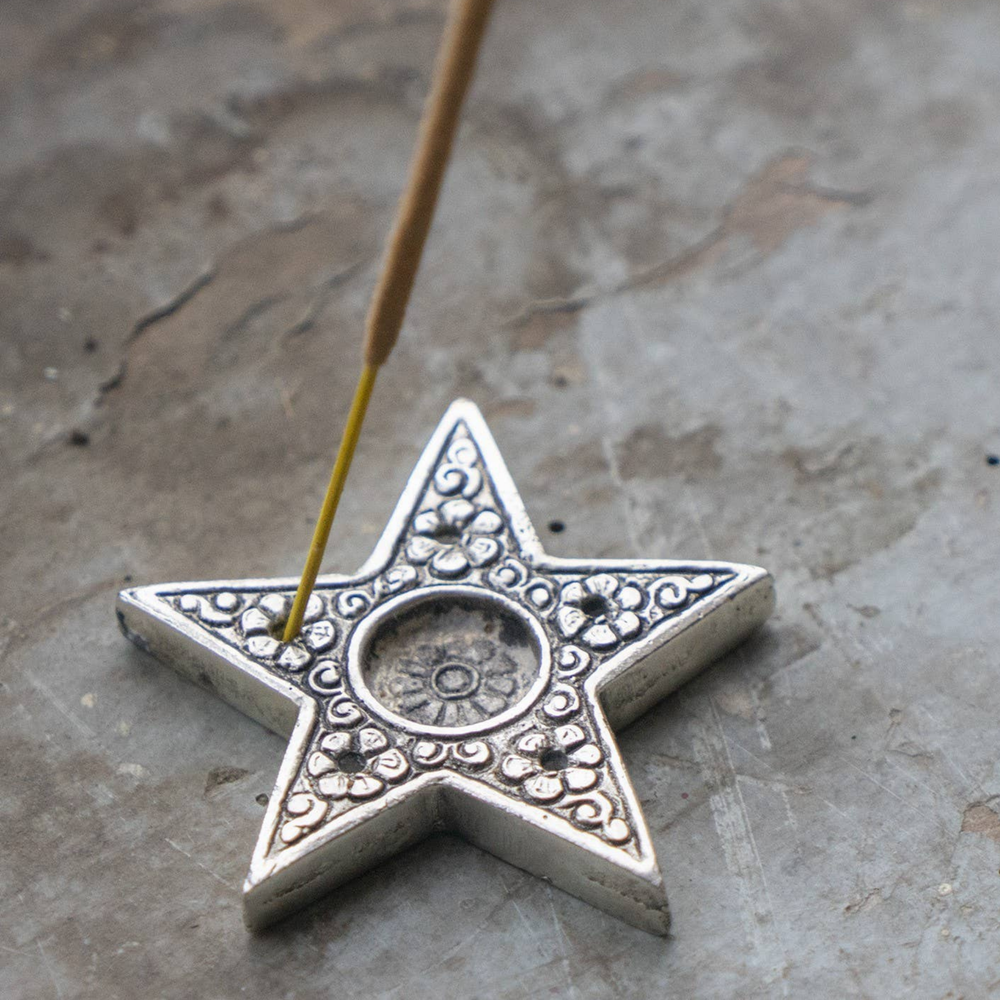 Decorative star-shaped incense holder with a lit incense stick on a textured surface