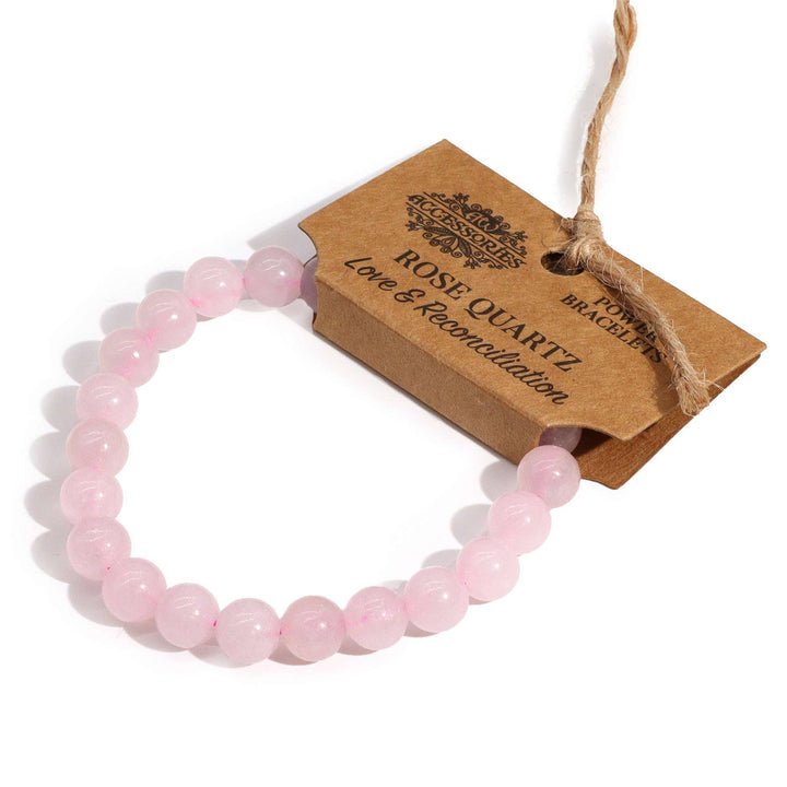 A pink bracelet made of rose quartz beads, displayed on a cardboard retail packaging with the brand name 'Ancient Wisdom'.