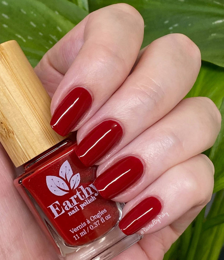Hand with red nail polish holding a bottle of Earthy nail polish.