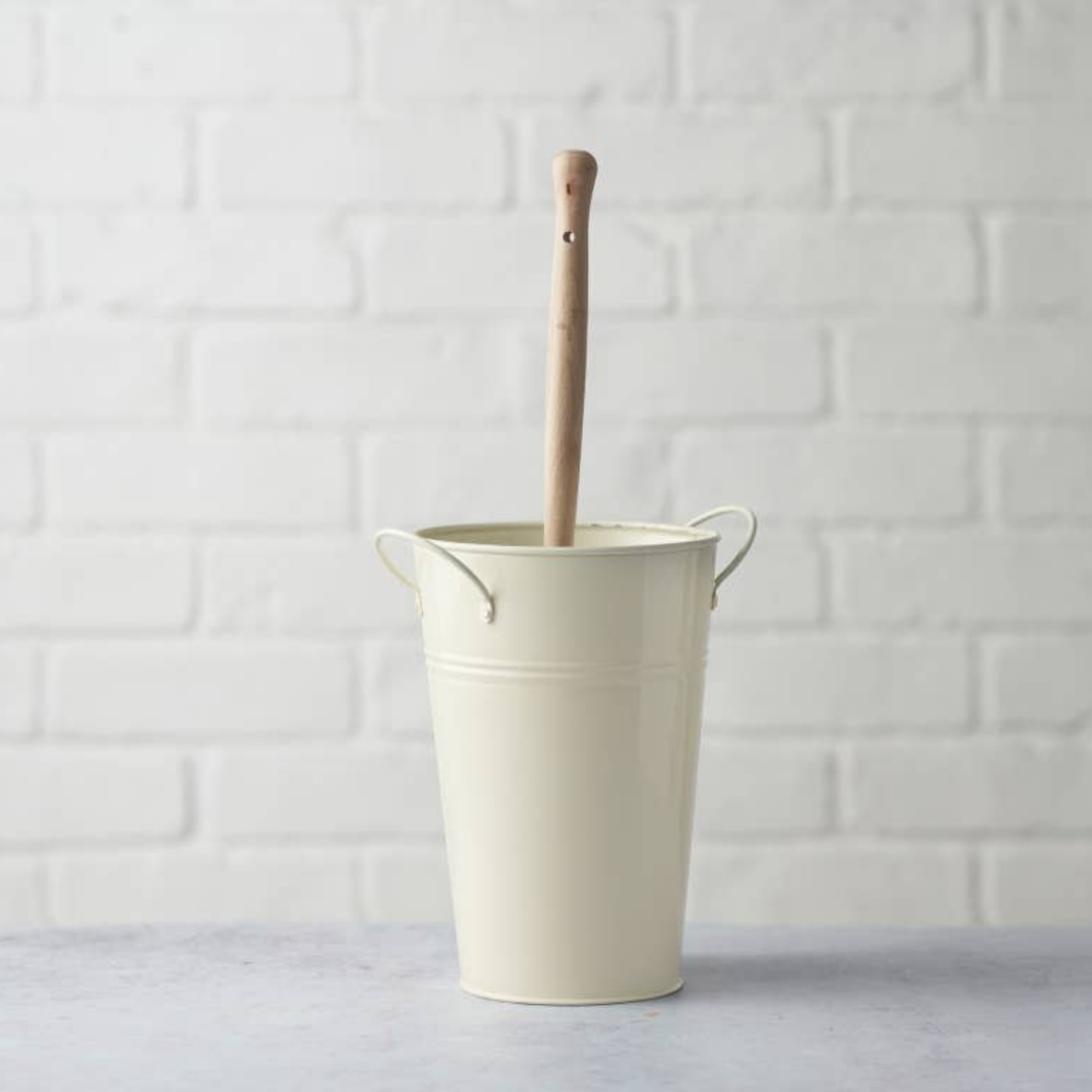 White bucket with a wooden handle on a light gray surface with a white tiled wall background