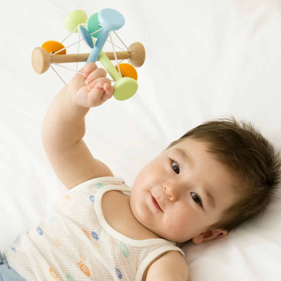 Baby lying on a white surface holding a colorful wooden toy