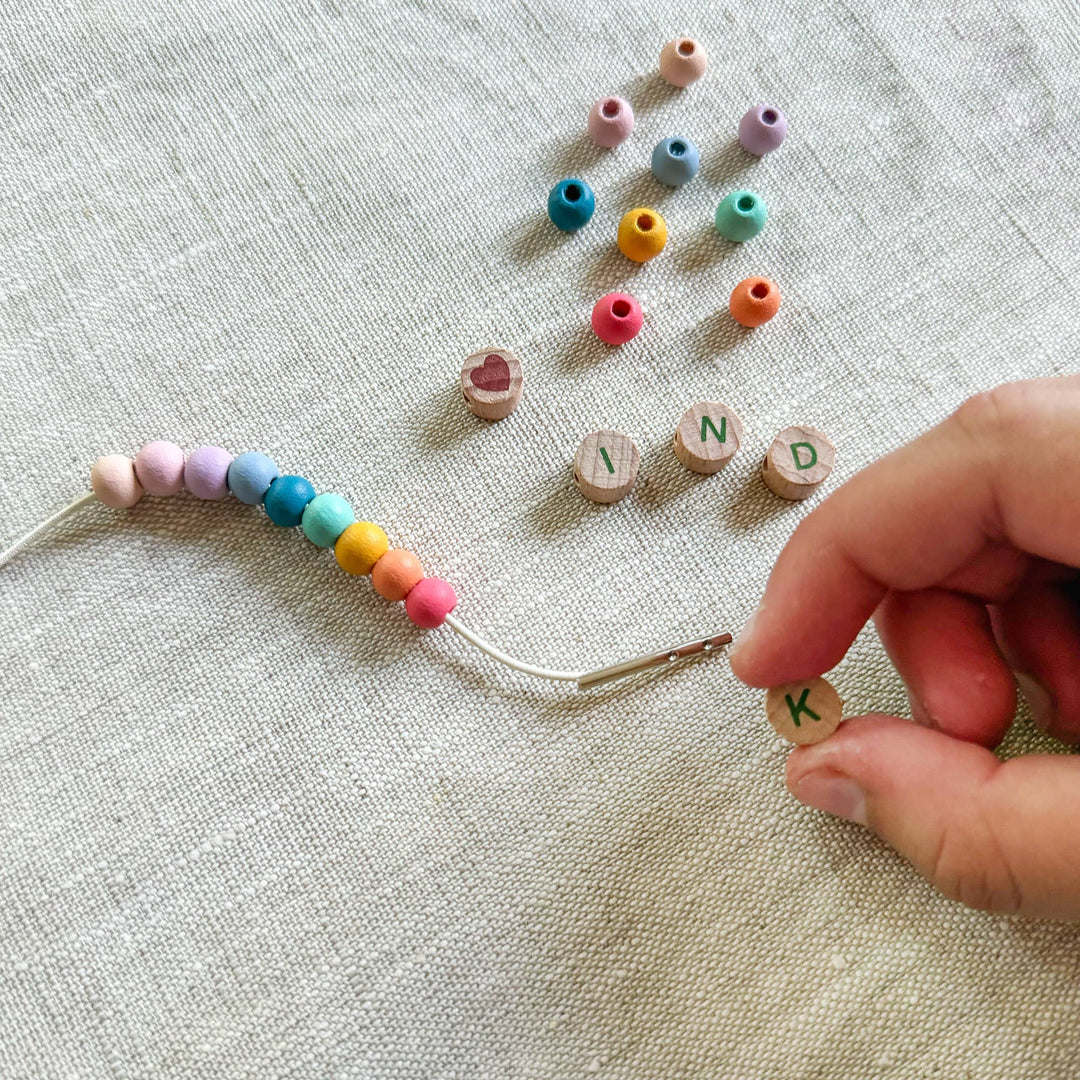 Hand holding a letter bead with colourful beaded string and scattered beads on a textured surface