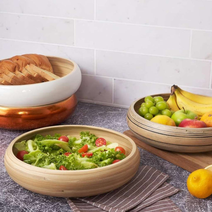 Bamboo bowls with salad, fruits, and bread on a kitchen counter.