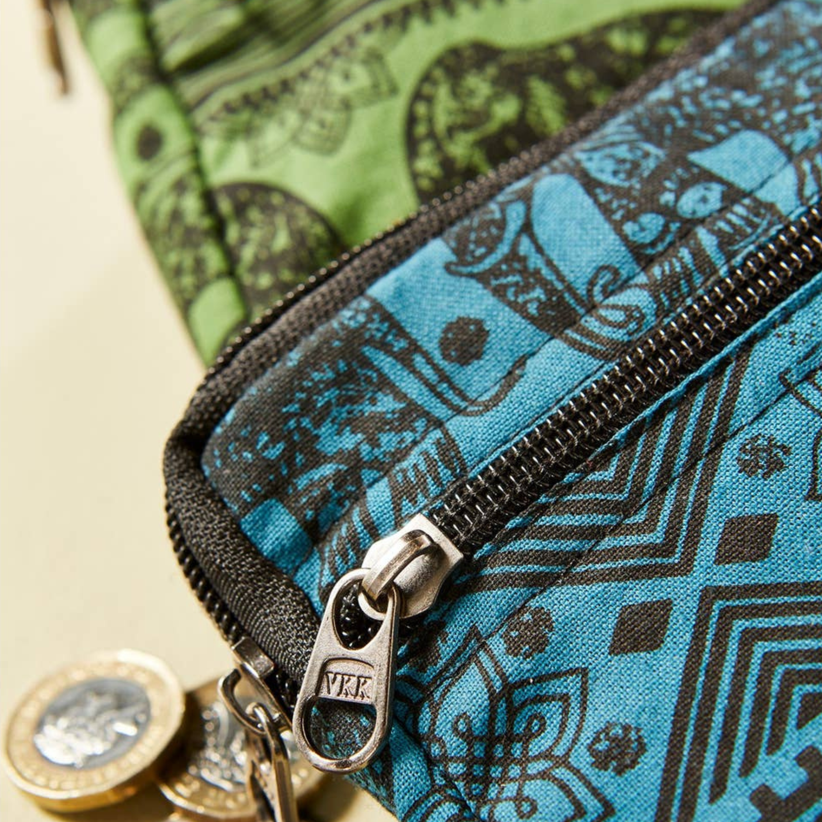 Three patterned coin purses, Blue, Green and purple with a black printed elephant design stacked on a beige background.