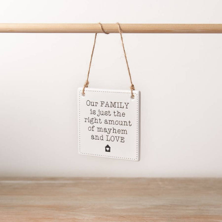 A chic engraved ceramic sign with a rustic jute string hanger with the phrase our family is just the right amount of mayhem and love. 