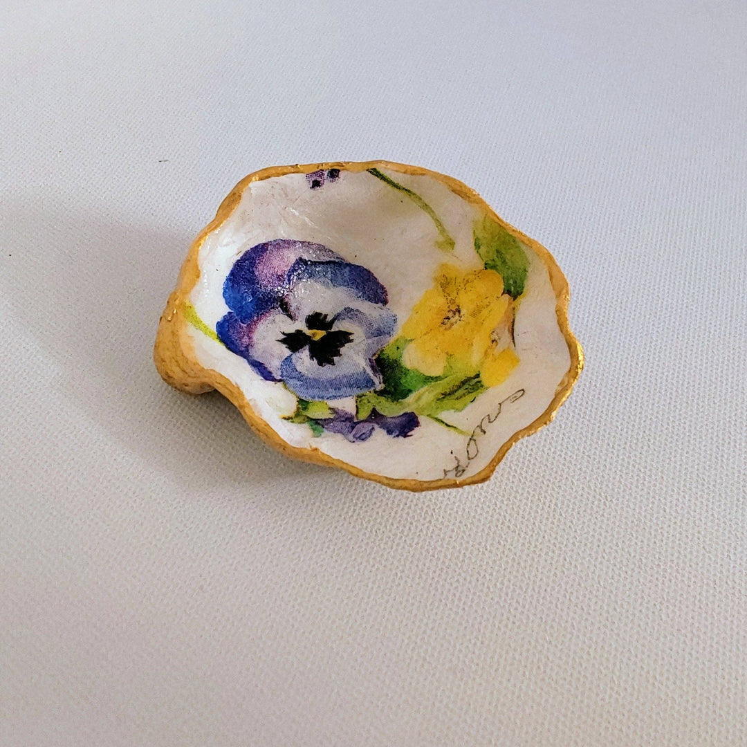 A hand-painted oyster shell trinket dish with gold edges, featuring a colorful floral pattern and the name 'Primrose' at the bottom.