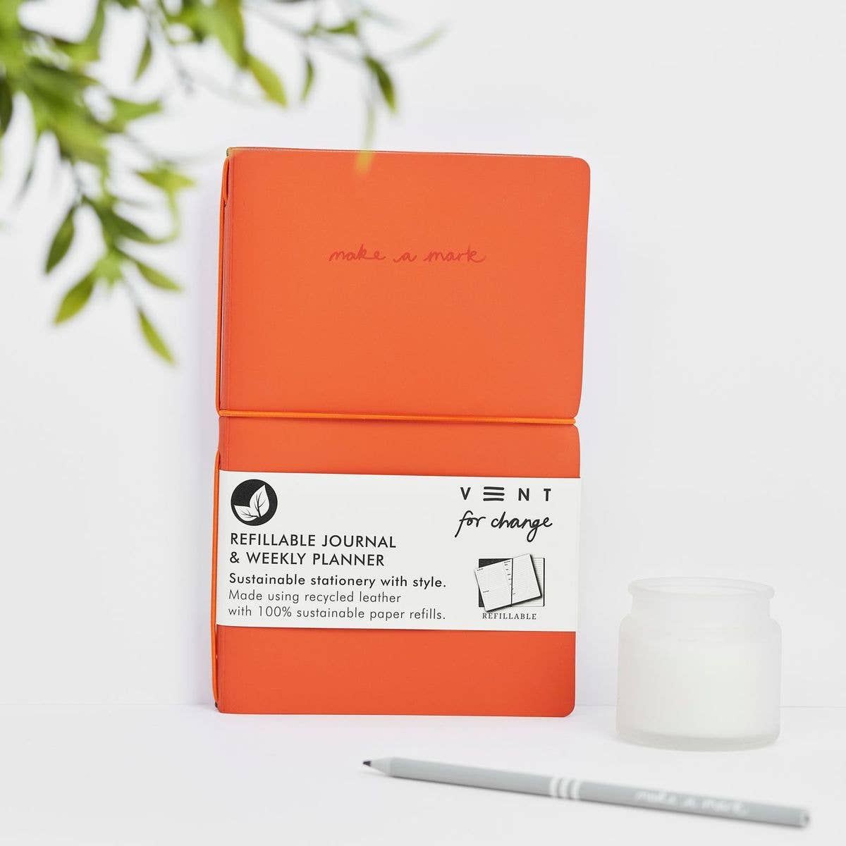 An orange refillable weekly planner and lined notes journal with a recycled leather cover, branded with 'VENT for Change' logo and made with sustainable paper.
